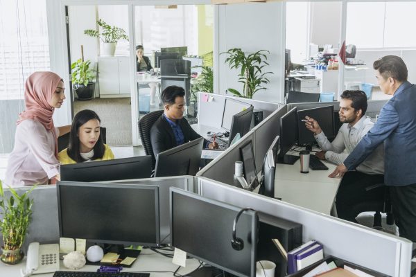 Busy office with men and women working at desks Multi racial businessmen and women using computers and discussing